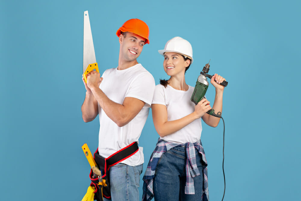 Ready For Repair. Smiling Couple In Protective Helmets Posing With Building Tools