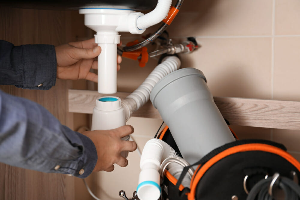Professional male plumber replacing sink trap indoors